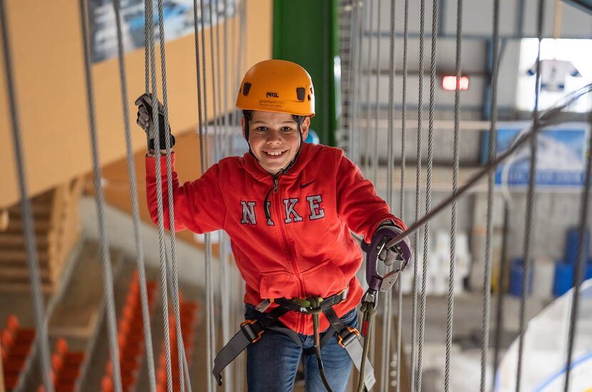 Zoom: Excursion en famille au parc d'escalade à cordes indoor de Grindelwald. Sous le toit de la patinoire, petits et grands peuvent se balancer et grimper sur des éléments plus ou moins branlants et passionnants, et ce par tous les temps : sec et sans vent en hiver, frais en été!