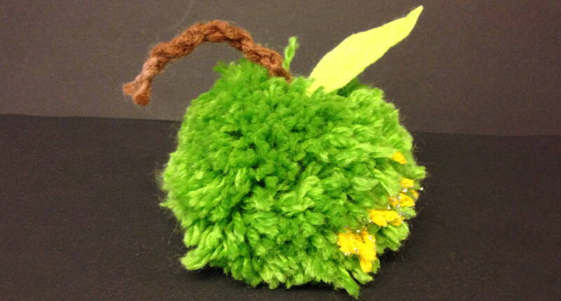 Selbstgemachter Apfelpompon aus Wolle zur Dekoration oder für die Kinderspielküche.